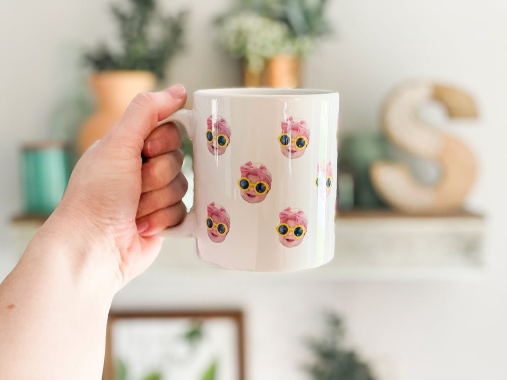 Person holding a mug with a baby's face multiplied around the mug in rows. Final product comes with images provided by customer. Shown in 11oz size.