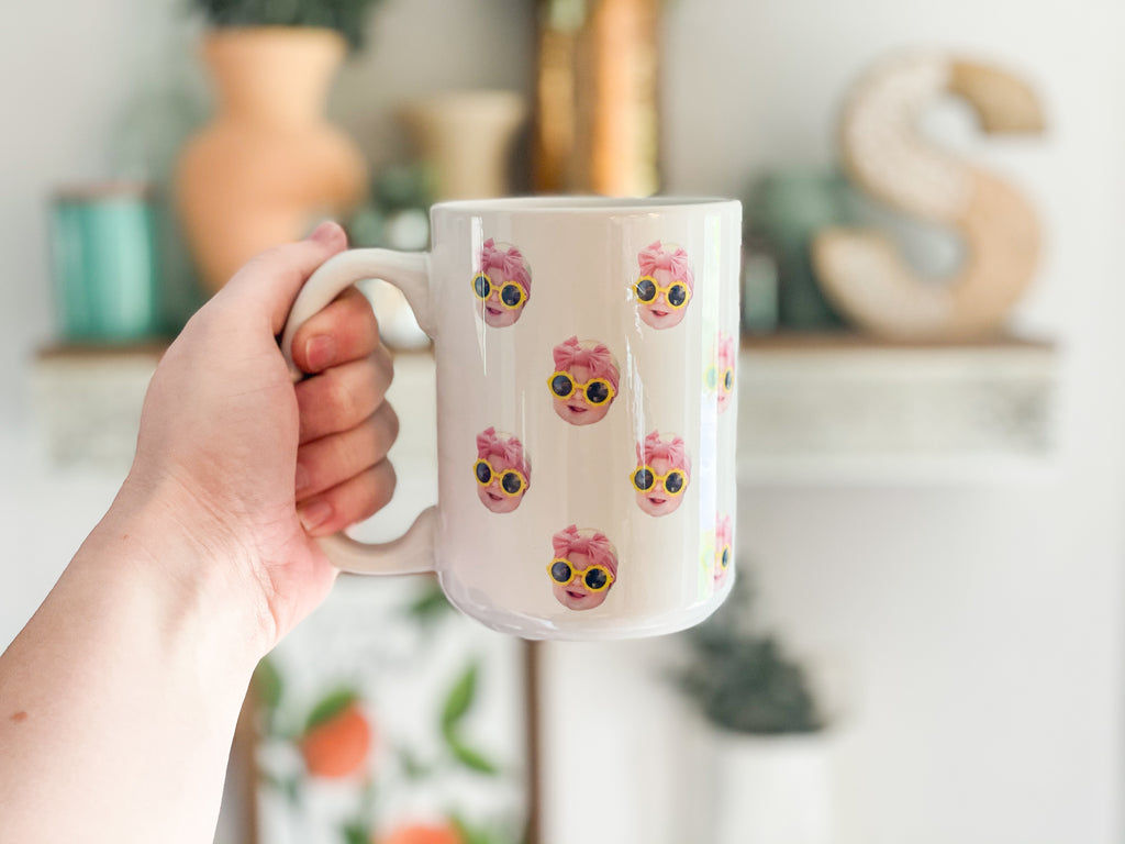 Person holding a mug with a baby's face multiplied around the mug in rows. Final product comes with images provided by customer. Shown in 15oz size.