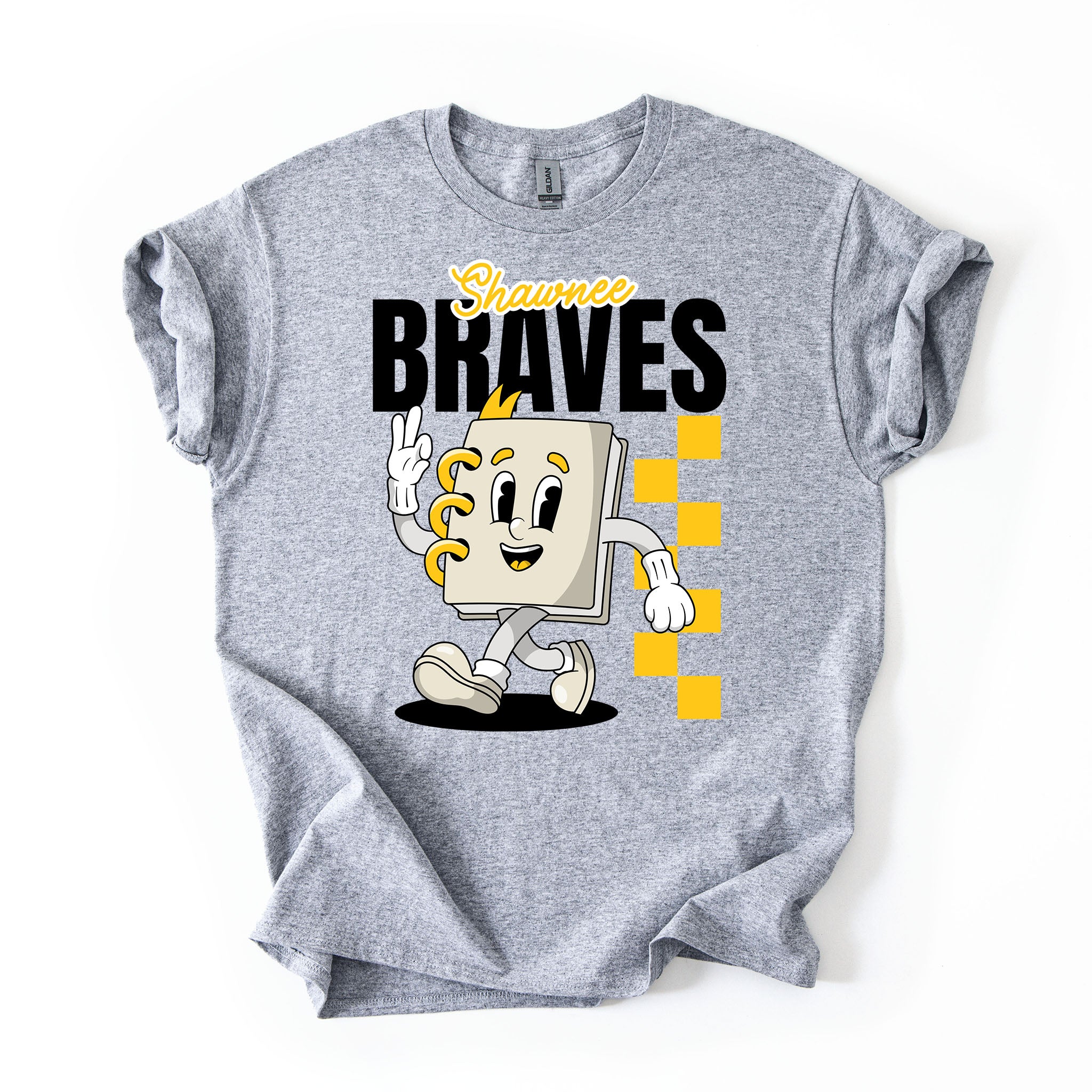 A heather gray short-sleeve t-shirt with a graphic print of a cartoon character notebook with yellow accents, the text 'Shawnee BRAVES' in black and yellow, and a yellow checkered pattern, shown on a plain white background.